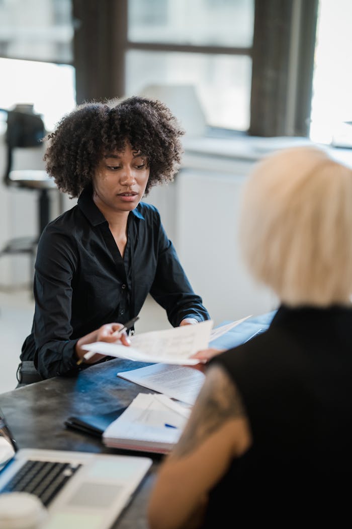 Two female professionals discussing documents in a modern office setting.