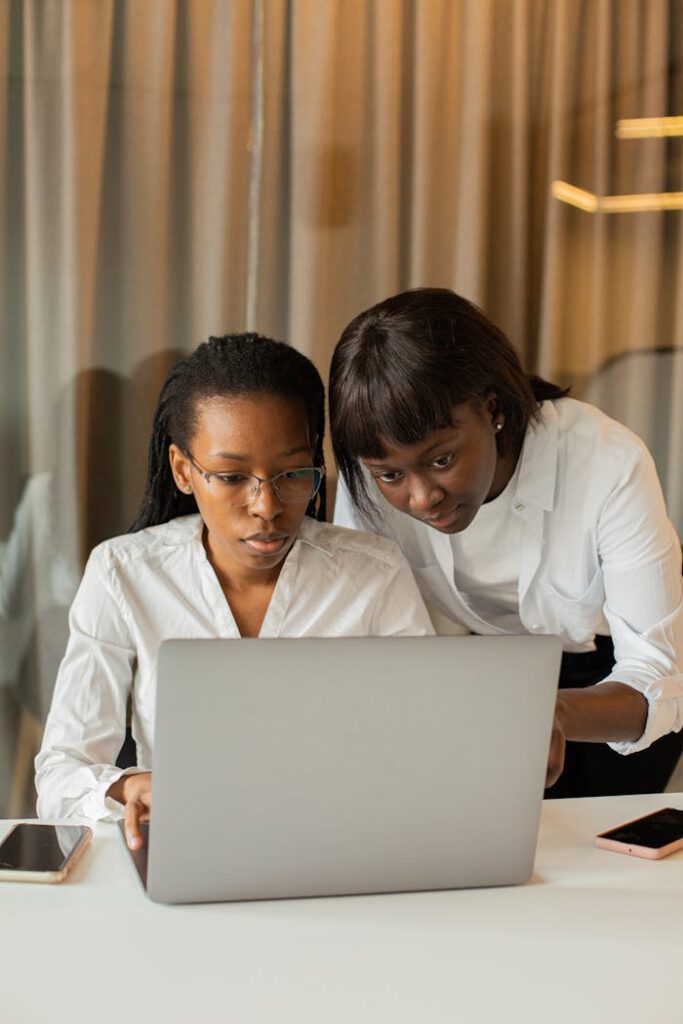 Two women in business attire working together on a laptop, fostering teamwork and cooperation.